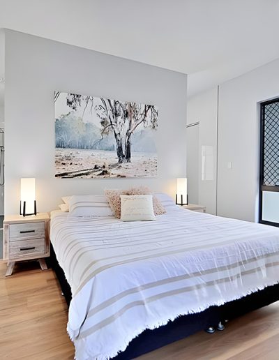 Bedroom with striped bedspread, gum tree artwork and large corner window
