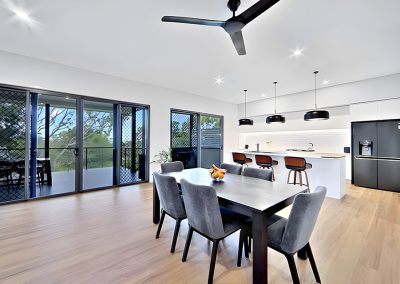 Dining area with grey chairs, black pendant lights and glass doors to a deck