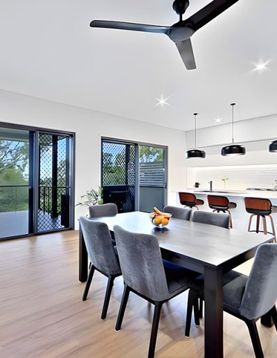 Dining area with grey chairs, black pendant lights and glass doors to a deck