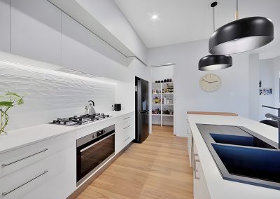 White galley kitchen with gas cooktop, black pendant lights and walk-in pantry