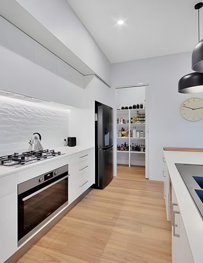 White galley kitchen with gas cooktop, black pendant lights and walk-in pantry