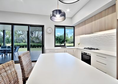 Kitchen with white island bench, textured white splashback and timber cabinets