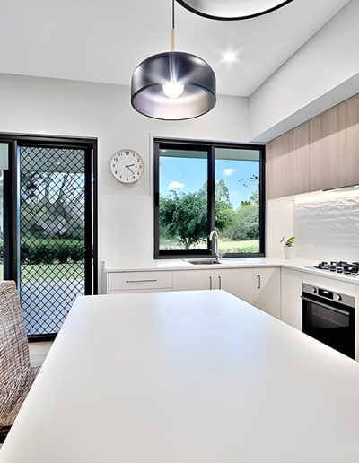 Kitchen with white island bench, textured white splashback and timber cabinets