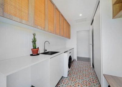 Laundry with rattan-front cabinets, white bench and patterned floor tiles