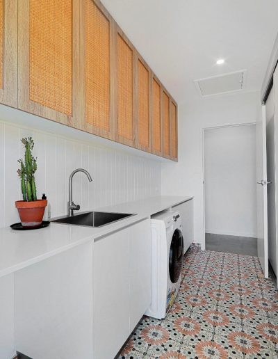 Laundry with rattan-front cabinets, white bench and patterned floor tiles