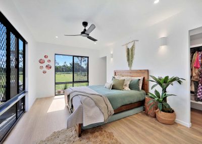 Bedroom with timber bed, green linen and a walk-in robe