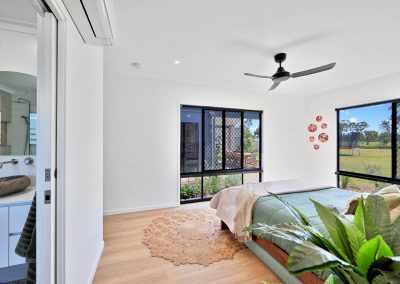 Bedroom with green bedding, ceiling fan and ensuite door open