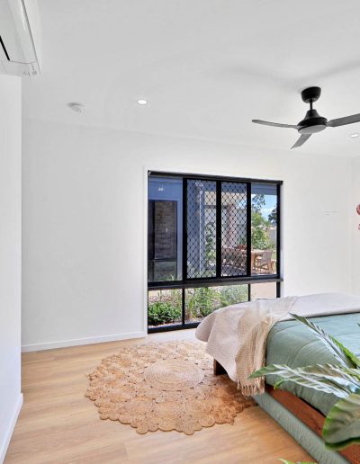 Bedroom with green bedding, ceiling fan and ensuite door open