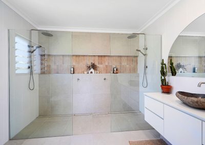 Walk-in double shower with tiled niche beside a stone basin vanity