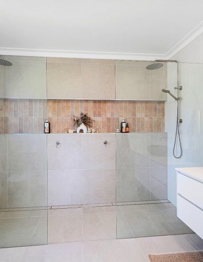 Walk-in double shower with tiled niche beside a stone basin vanity