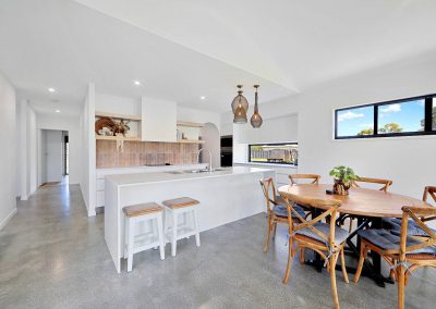 Kitchen bench with white stools beside a round timber dining table