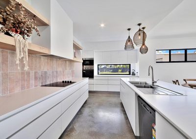 White kitchen with pink tile splashback, induction cooktop and woven pendant lights