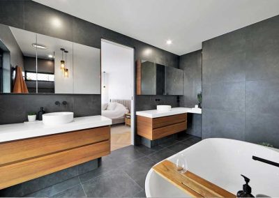 Dark-tiled bathroom with timber-look double vanity and freestanding bath