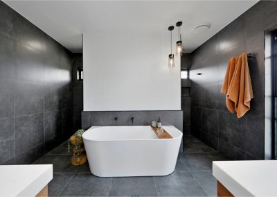 Freestanding bath against a half-height wall in a dark-tiled bathroom