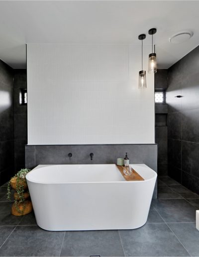 Freestanding bath against a half-height wall in a dark-tiled bathroom