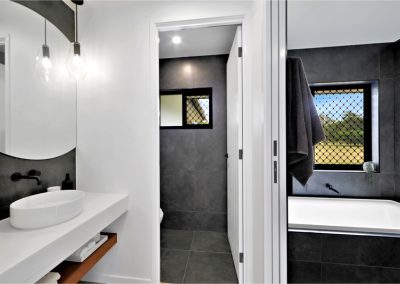 Bathroom with round mirror, vessel basin and dark-tiled bath area