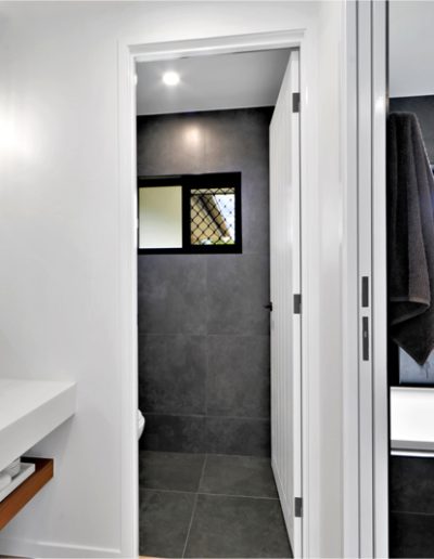 Bathroom with round mirror, vessel basin and dark-tiled bath area