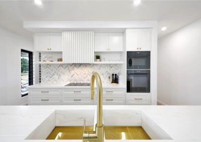 Kitchen with brass sink and tap, herringbone splashback and black wall ovens