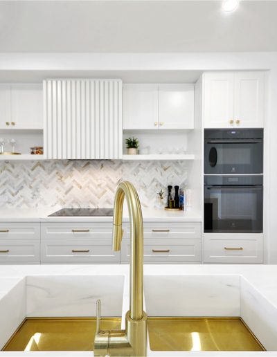 Kitchen with brass sink and tap, herringbone splashback and black wall ovens