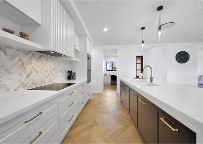 White kitchen with herringbone splashback, brass handles and dark timber island