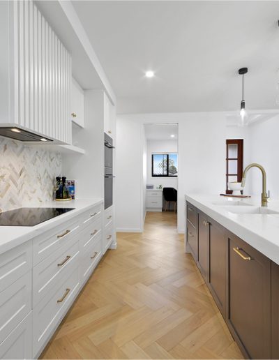 White kitchen with herringbone splashback, brass handles and dark timber island