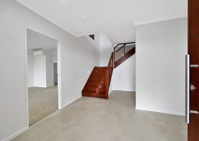 Tiled entry hall and timber staircase seen past the open front door