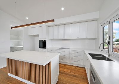 White kitchen with timber-slatted island, timber pendant light and window over the sink