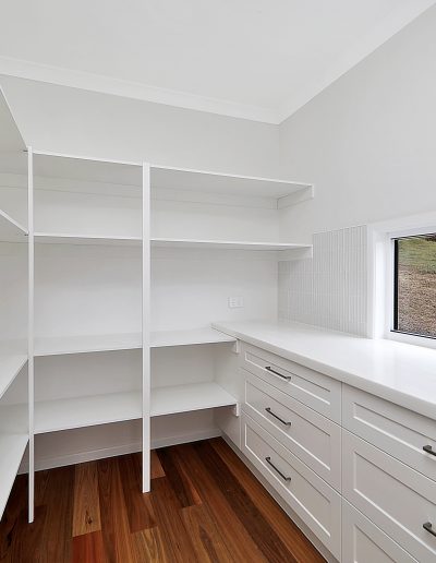 Walk-in pantry with open white shelves and a bank of drawers