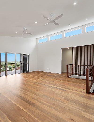 Living area with timber floors, high windows and slatted stair screen