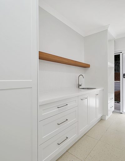 White cabinetry with sink, drawers and a floating timber shelf